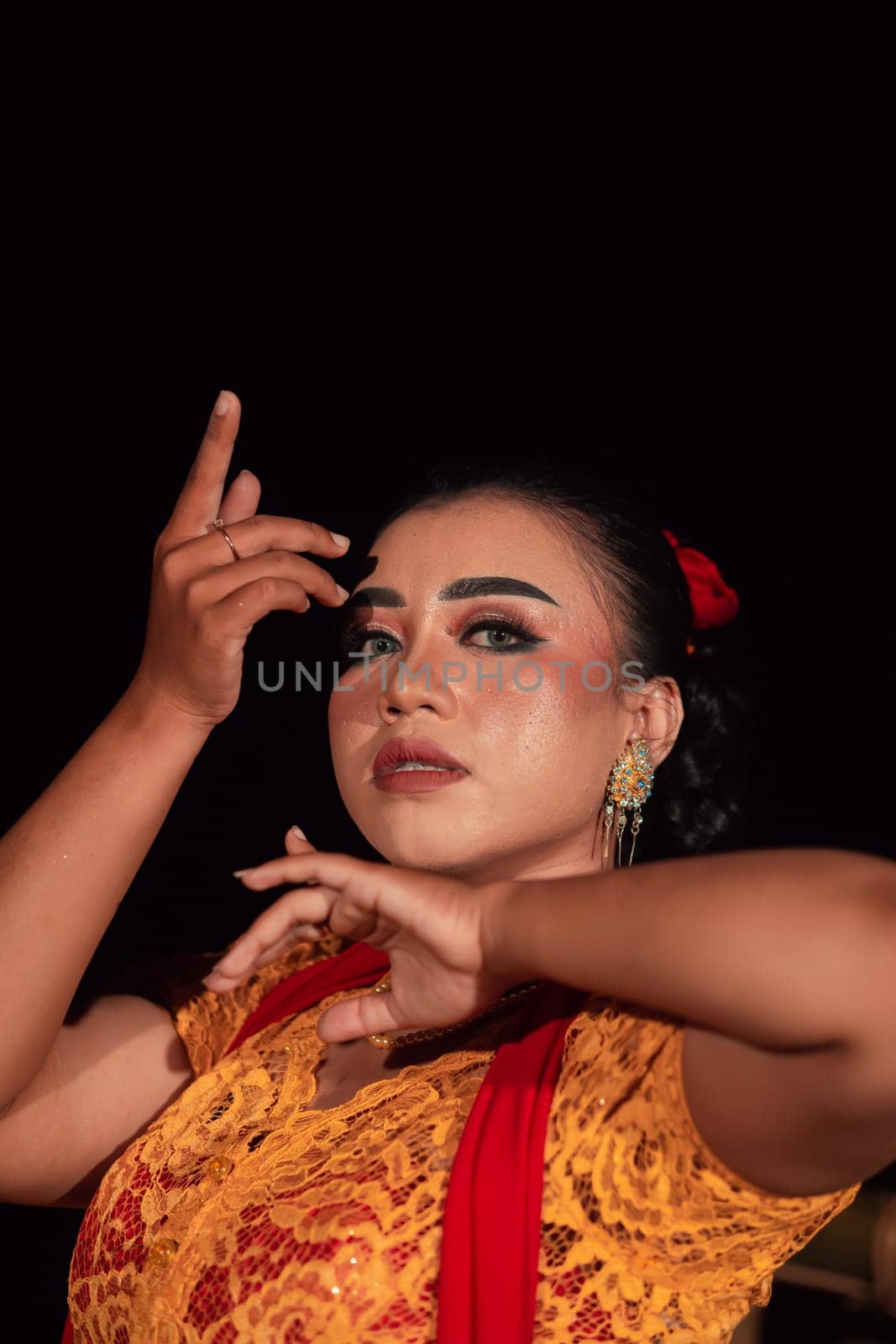 the fierce face of a Balinese woman with makeup in a traditional orange dress and red scarf while dancing at the festival in the night
