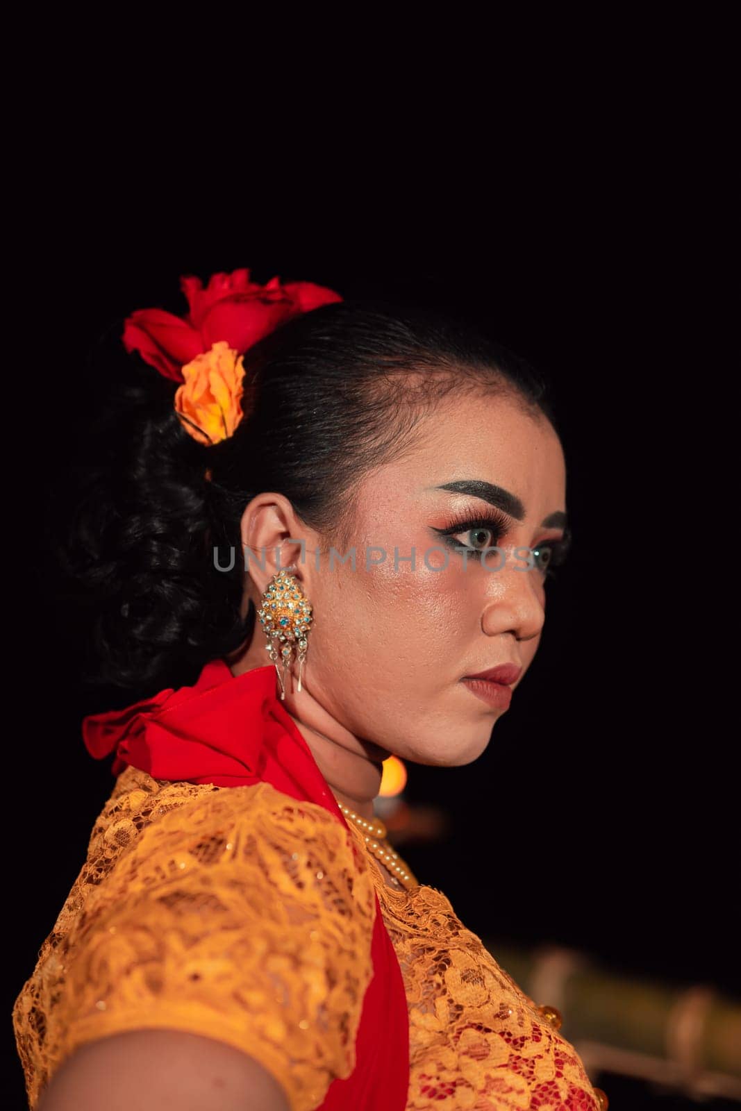 Javanese woman in a traditional orange dress while wearing makeup and a red scarf at a dance festival in Indonesia