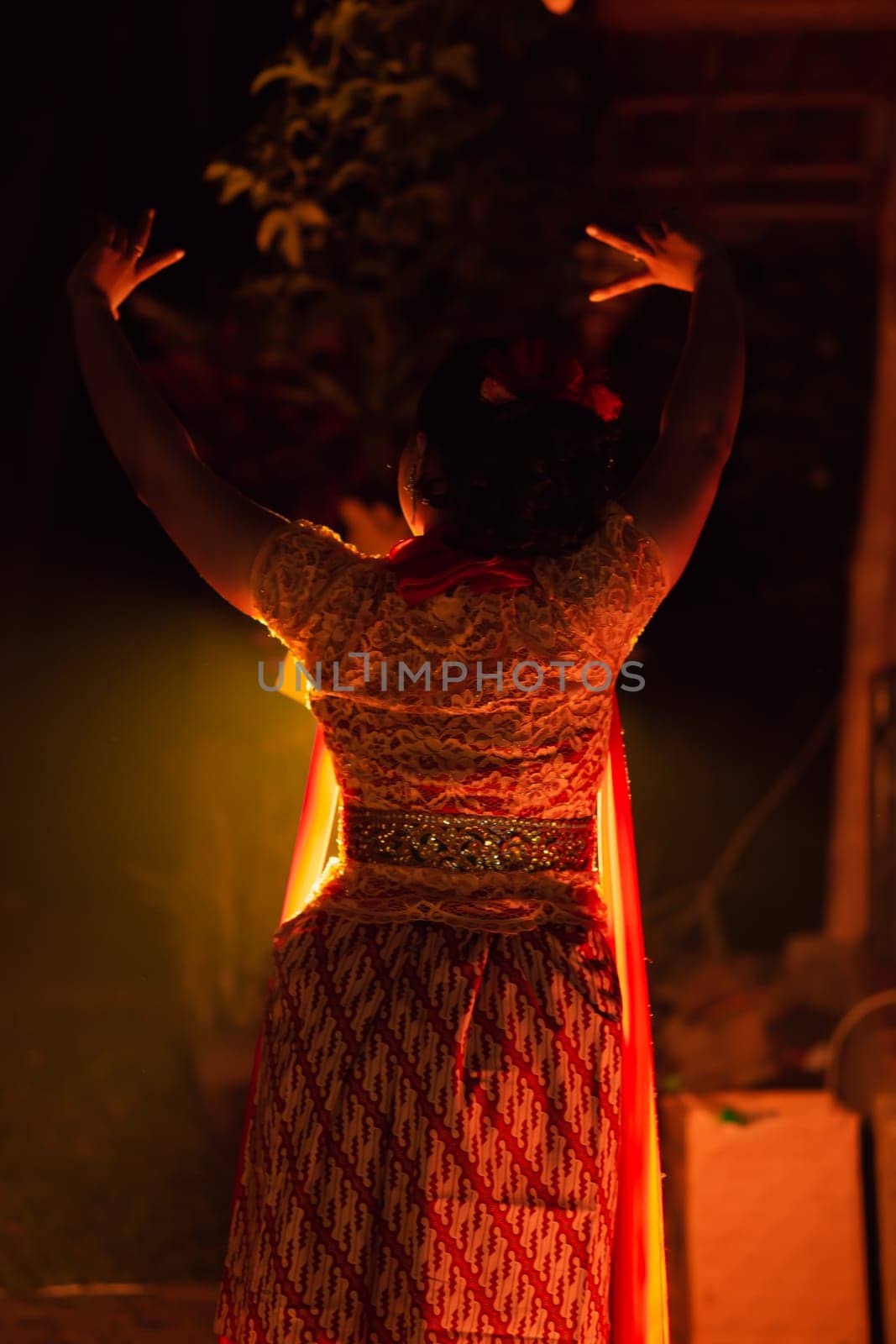 A Silhouette body of a Balinese woman in a traditional orange dress while dancing in front of the lighting on the dark night at the festival