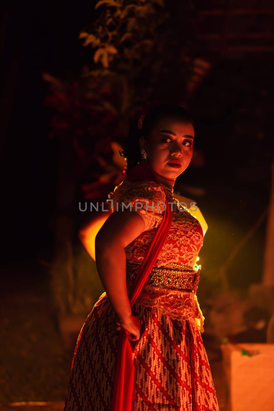 A Silhouette body of a Balinese woman in a traditional orange dress while dancing in front of the lighting on the dark night at the festival