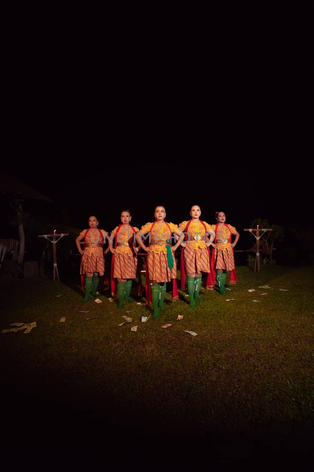 Balinese dancers standing together with red scarf and orange costumes on the stage after performing the traditional dance at the festival
