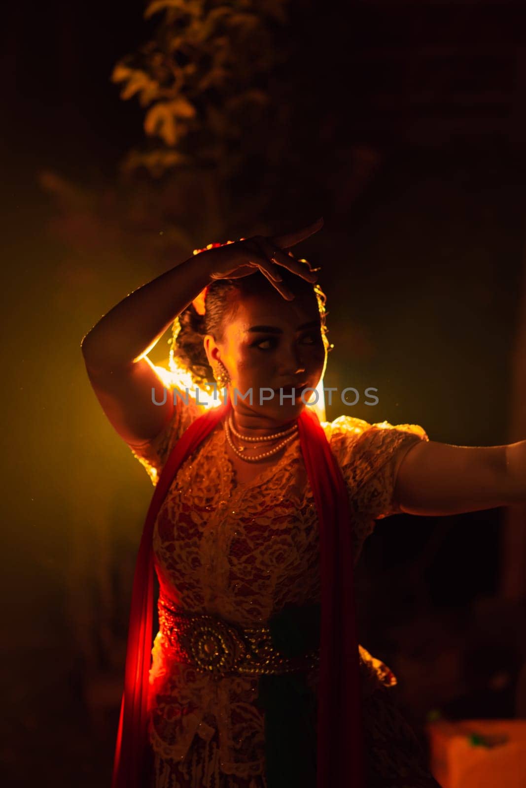 A Silhouette body of a Balinese woman in a traditional orange dress while dancing in front of the lighting on the dark night at the festival