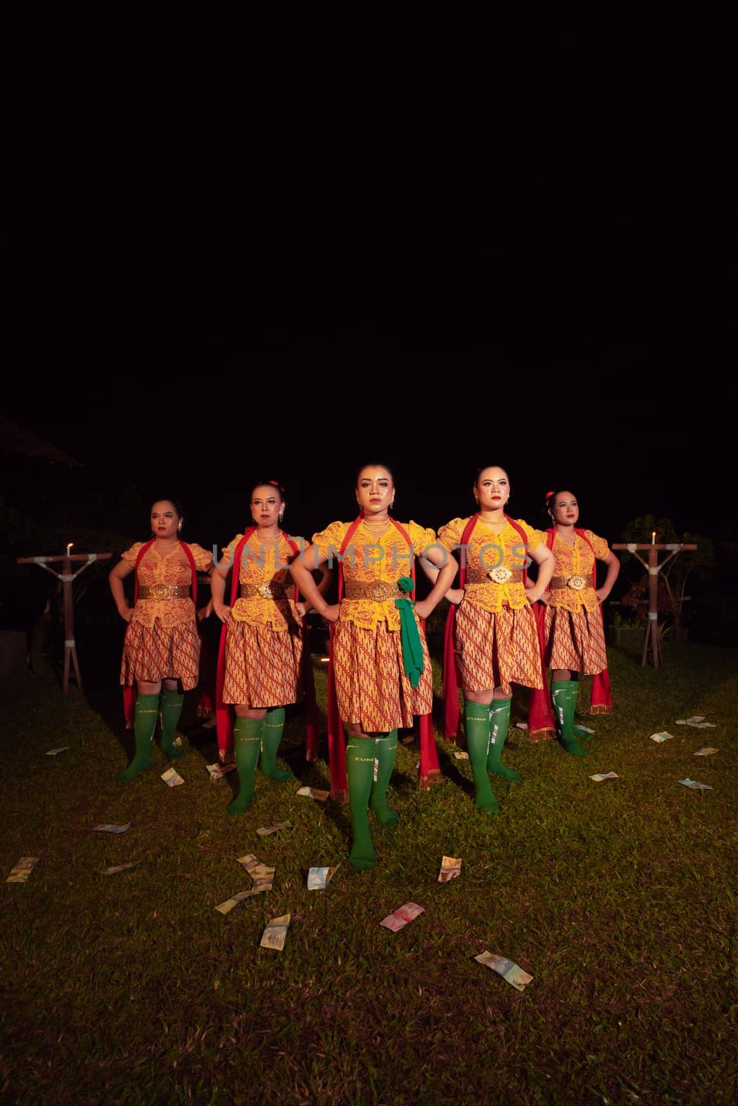Balinese dancers standing together with red scarf and orange costumes on the stage after performing the traditional dance at the festival
