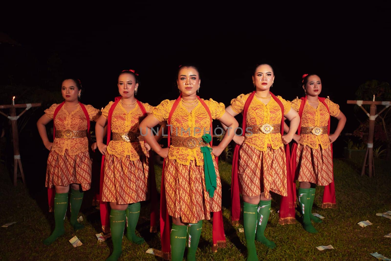 Balinese dancers standing together with red scarf and orange costumes on the stage after performing the traditional dance at the festival