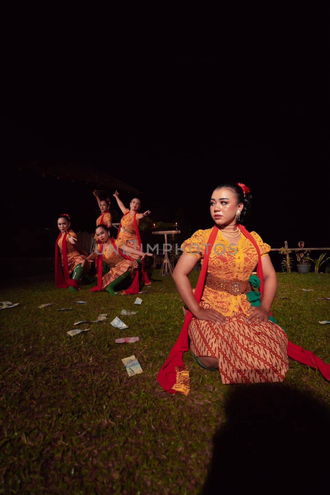A Group of Indonesian dancers performing on the stage with a red scarf and traditional orange dress inside the festival during the night