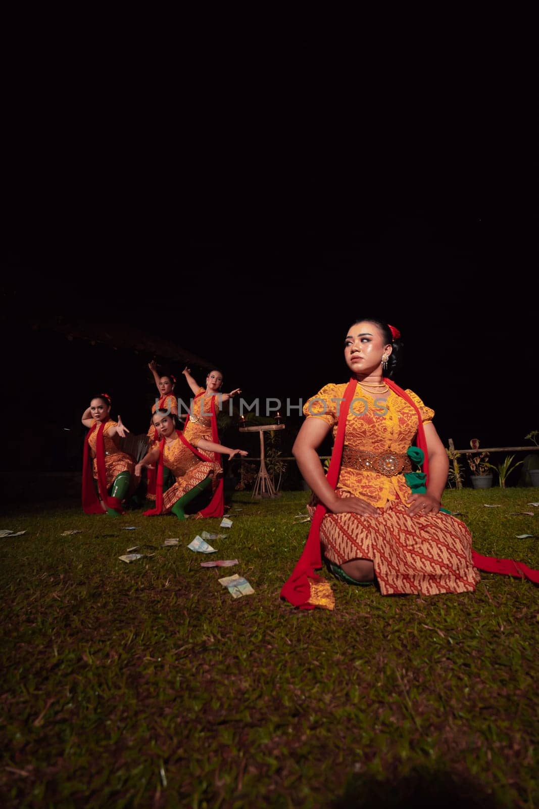 A Group of Indonesian dancers performing on the stage with a red scarf and traditional orange dress inside the festival during the night
