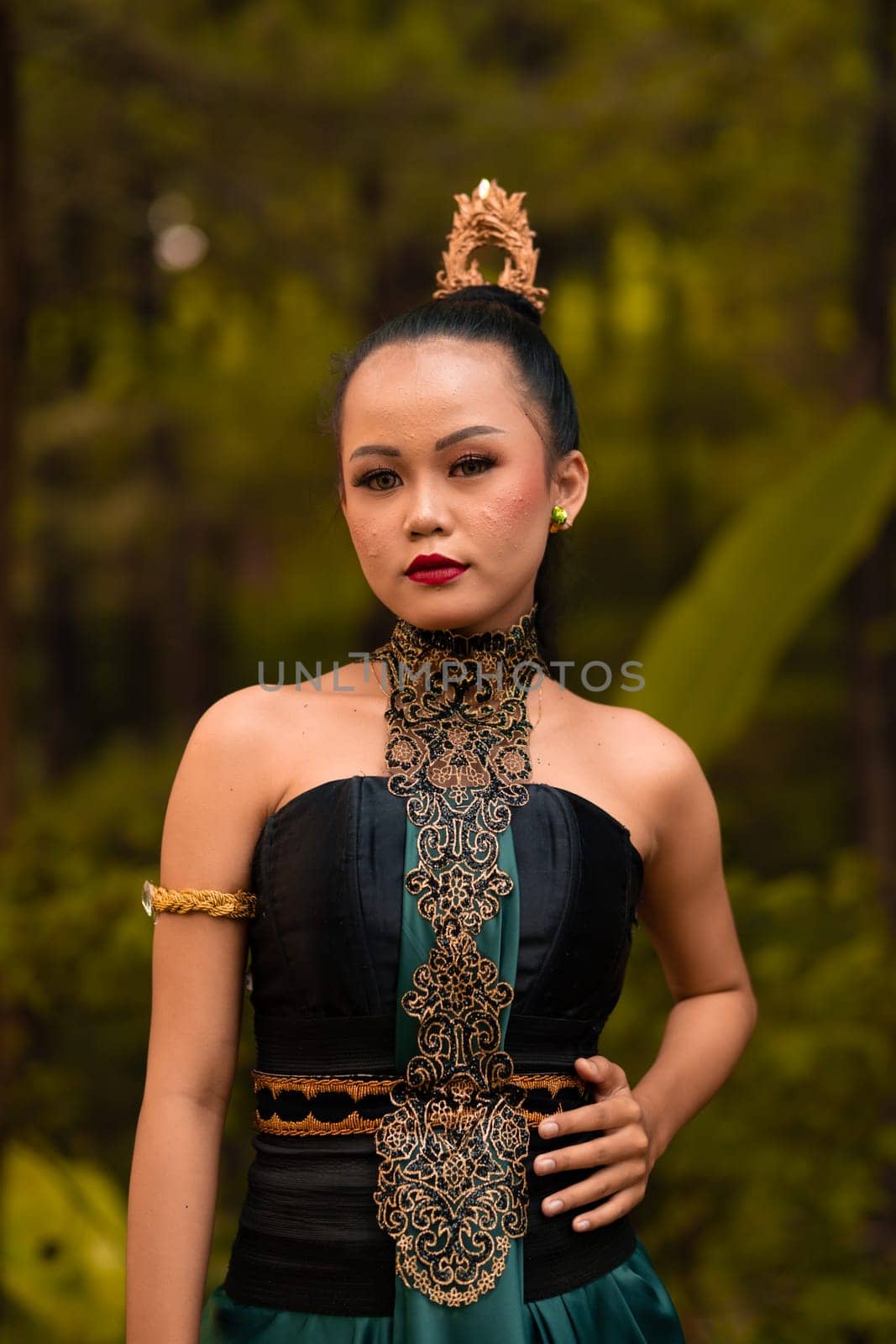 Indonesian woman with the green dress and make-up on her face standing in front of the jungle during the dance festival