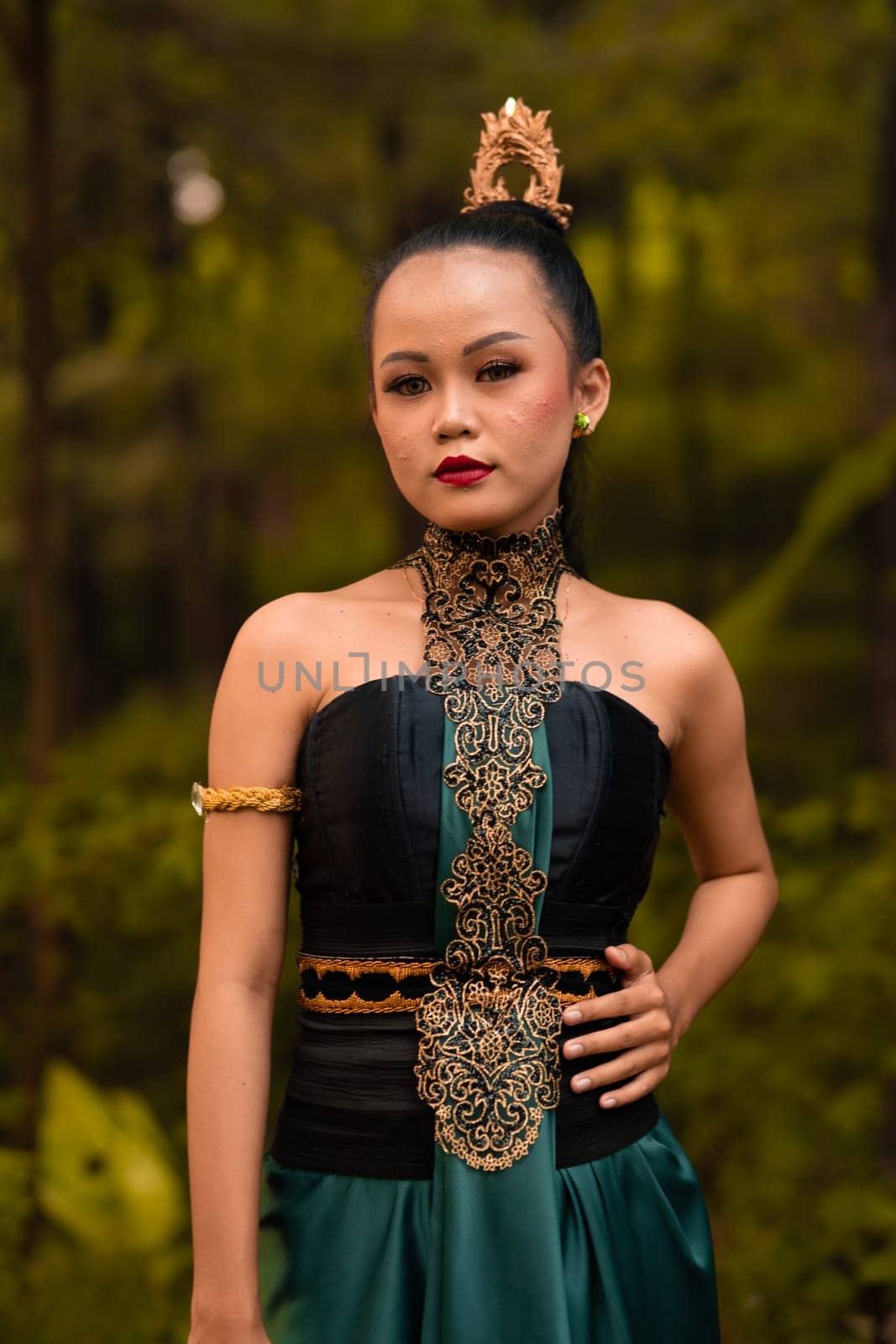 Indonesian woman with the green dress and make-up on her face standing in front of the jungle during the dance festival