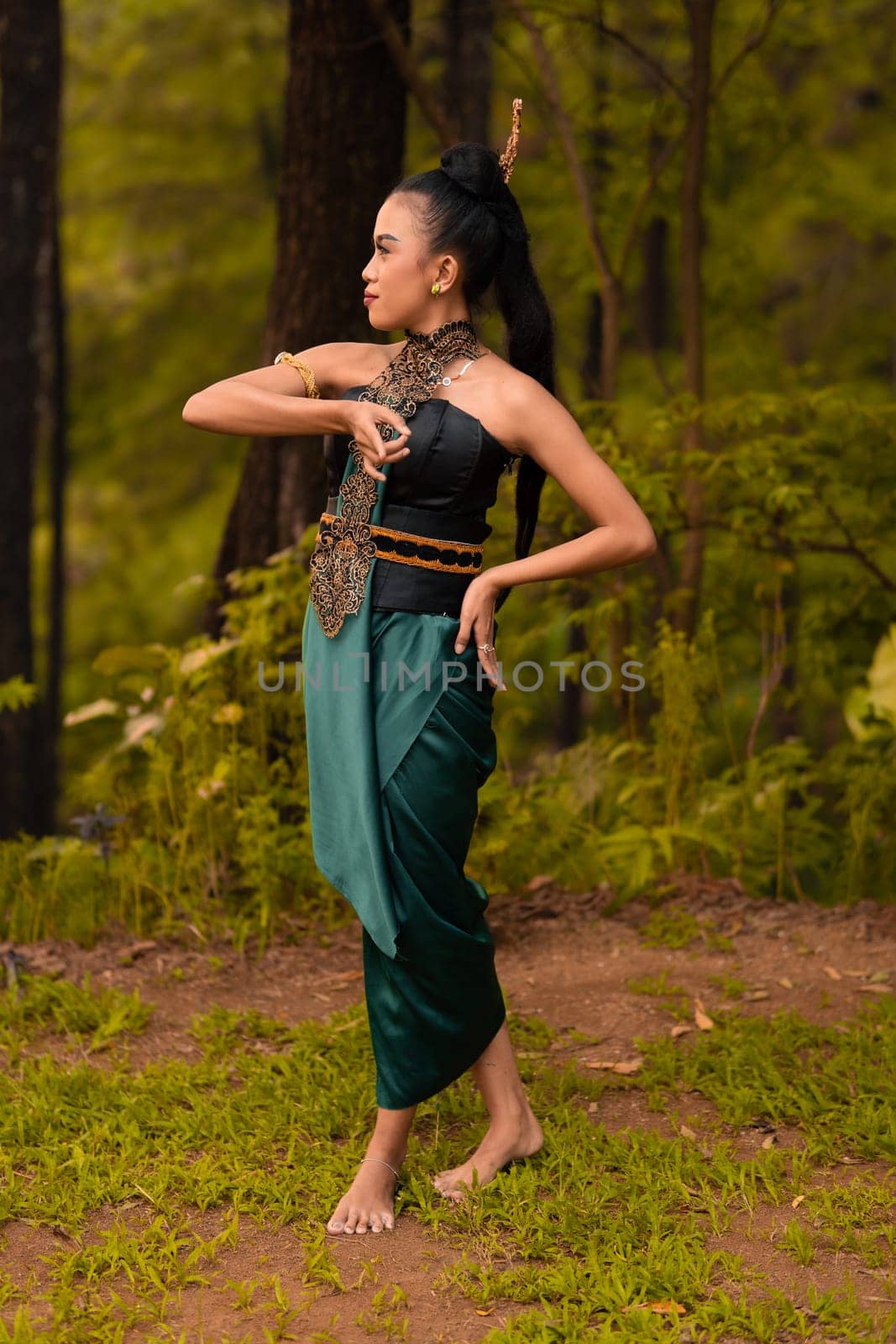 Beautiful Indonesian dancers with traditional green costumes and black tied hair posing inside the forest after performing