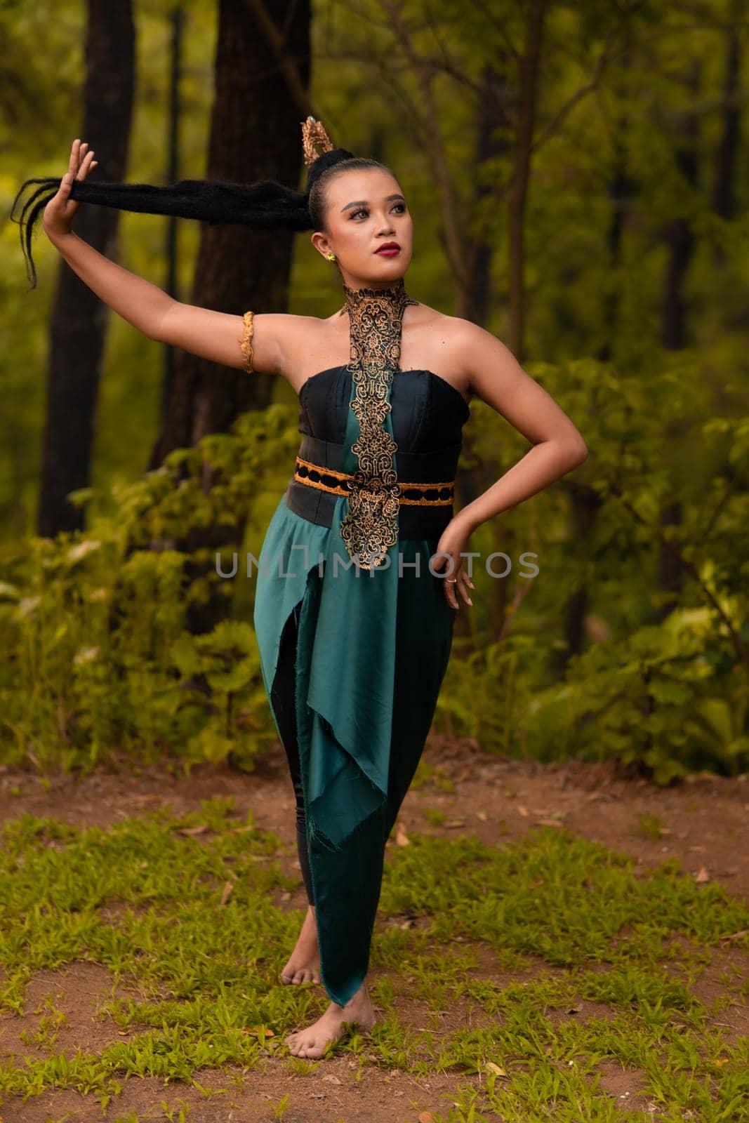 Beautiful Asian woman holding her black hair while standing in front of the forest in a green costume during the festival
