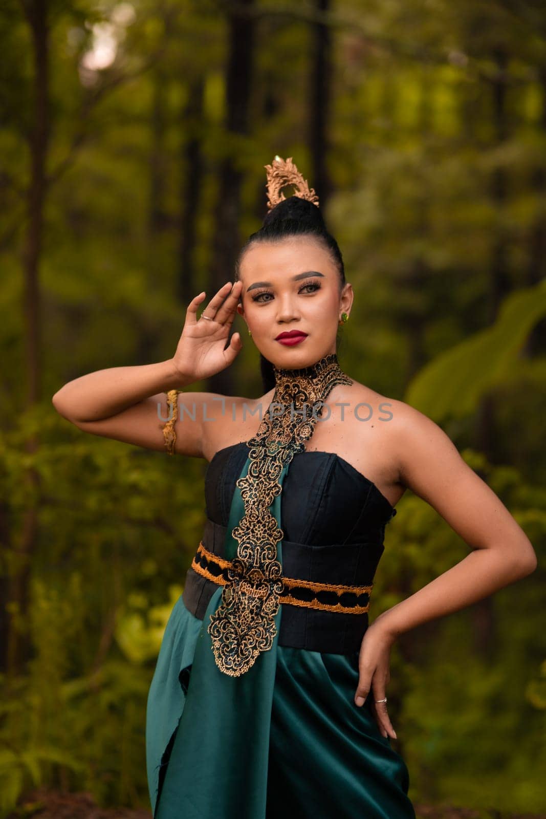 Beautiful Indonesian woman with a green dress and makeup on her face posing in front of the forest with their hand during the morning