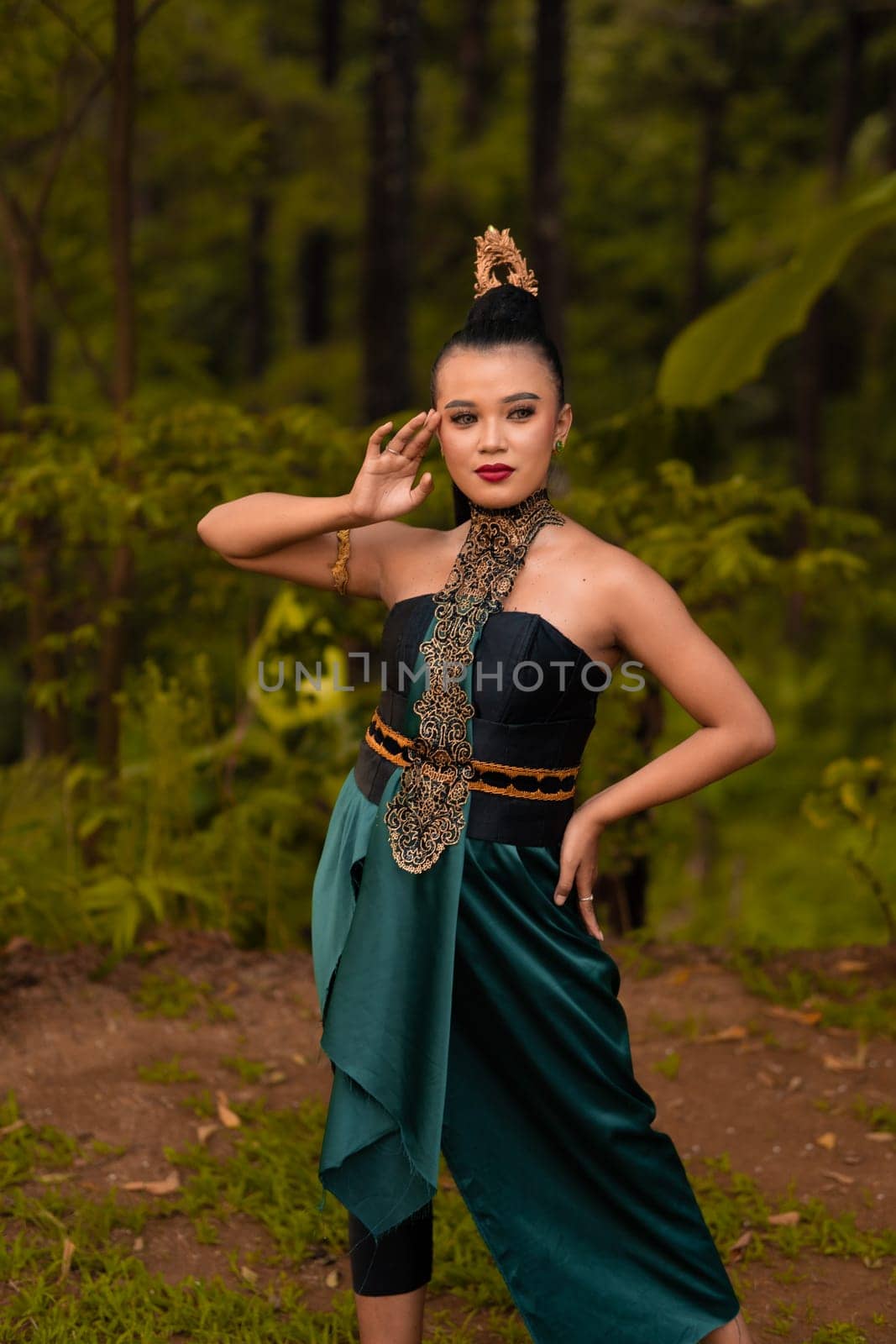 Beautiful Indonesian woman with a green dress and makeup on her face posing in front of the forest with their hand during the morning