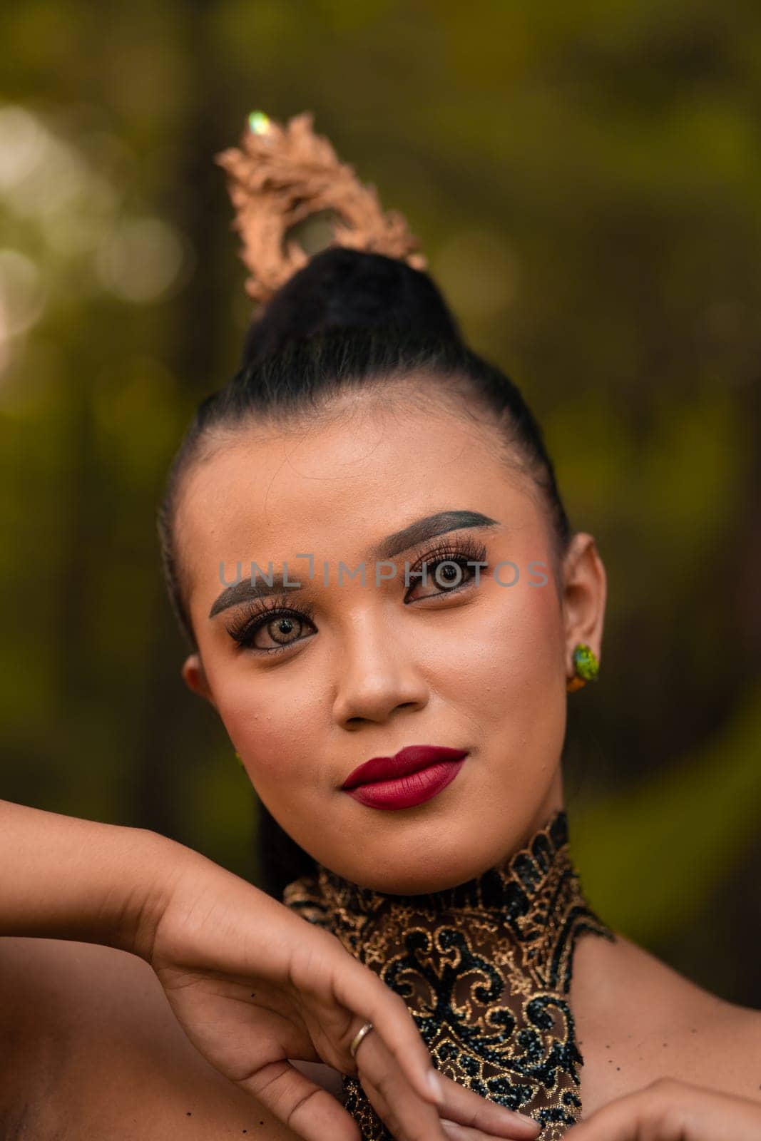 Beautiful eyes of an Asian woman in makeup and red lipstick while wearing gold jewelry and black hair while standing in front of the jungle