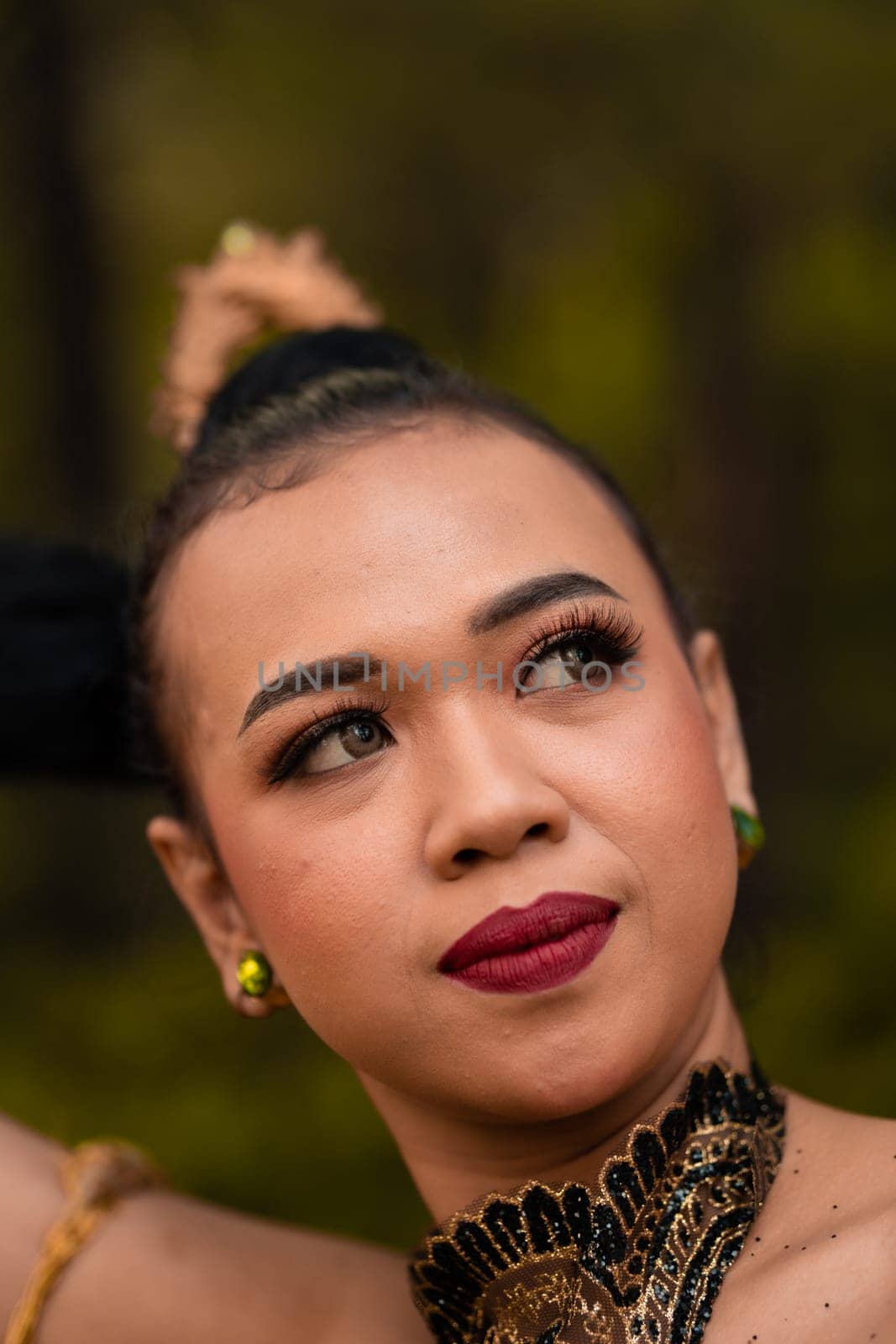 Close-up face of an Asian woman in makeup with red lips and a golden black necklace inside the forest