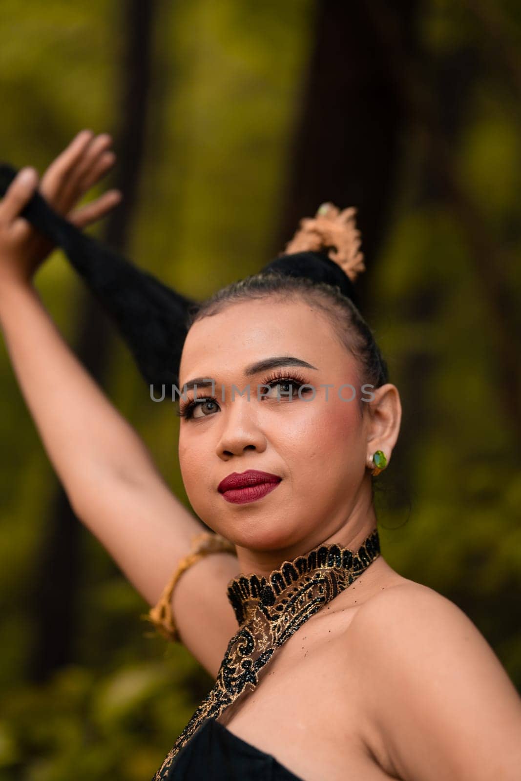 Asian woman holding her black hair in a green costume while wearing makeup and posing in front of the forest during the dance festival inside the village