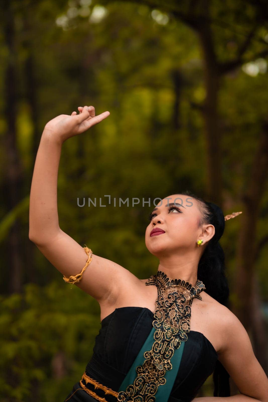 Balinese women raise their hands in the air while dancing in green costumes while performing in the festival in front of the jungle