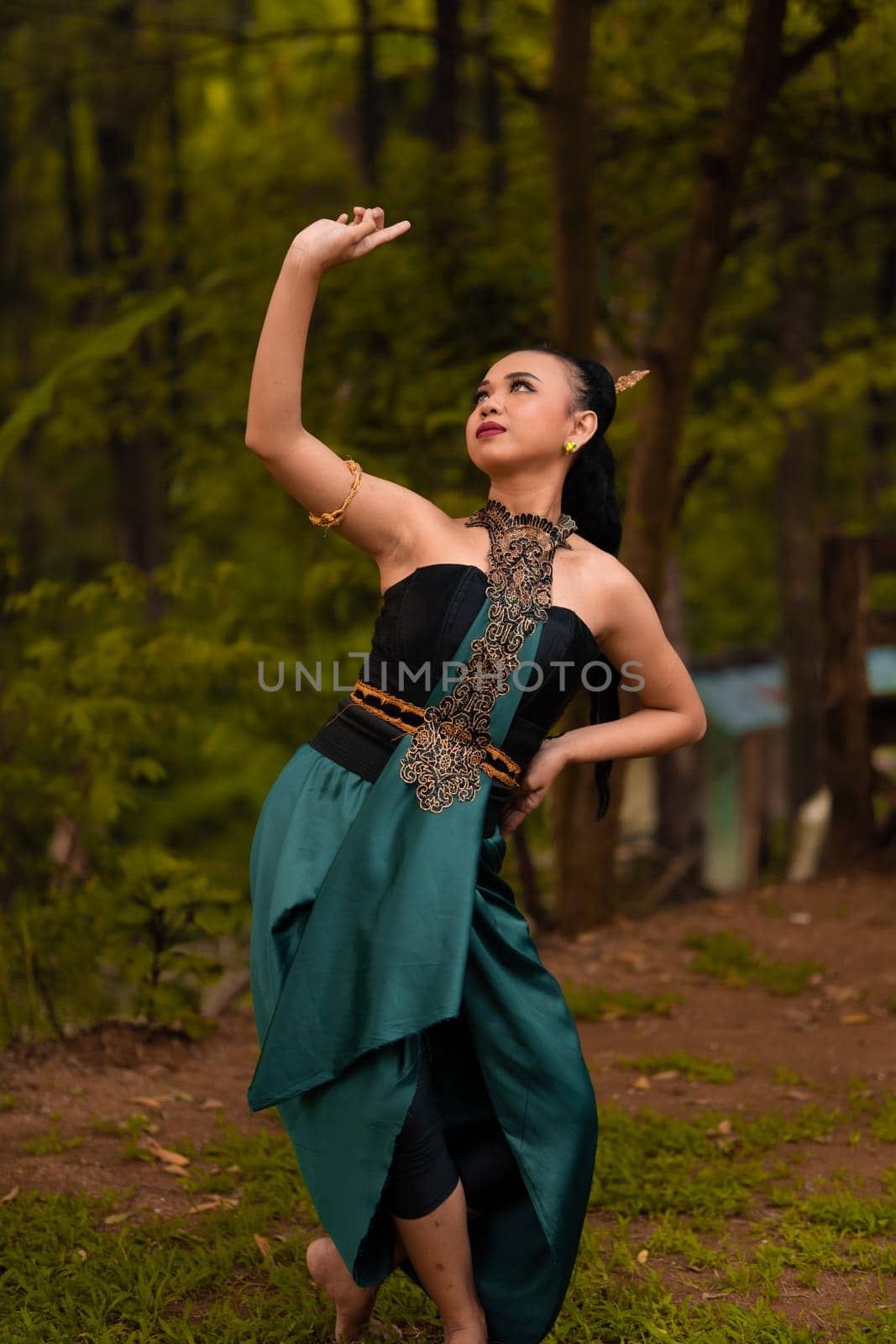 Balinese women raise their hands in the air while dancing in green costumes while performing in the festival in front of the jungle