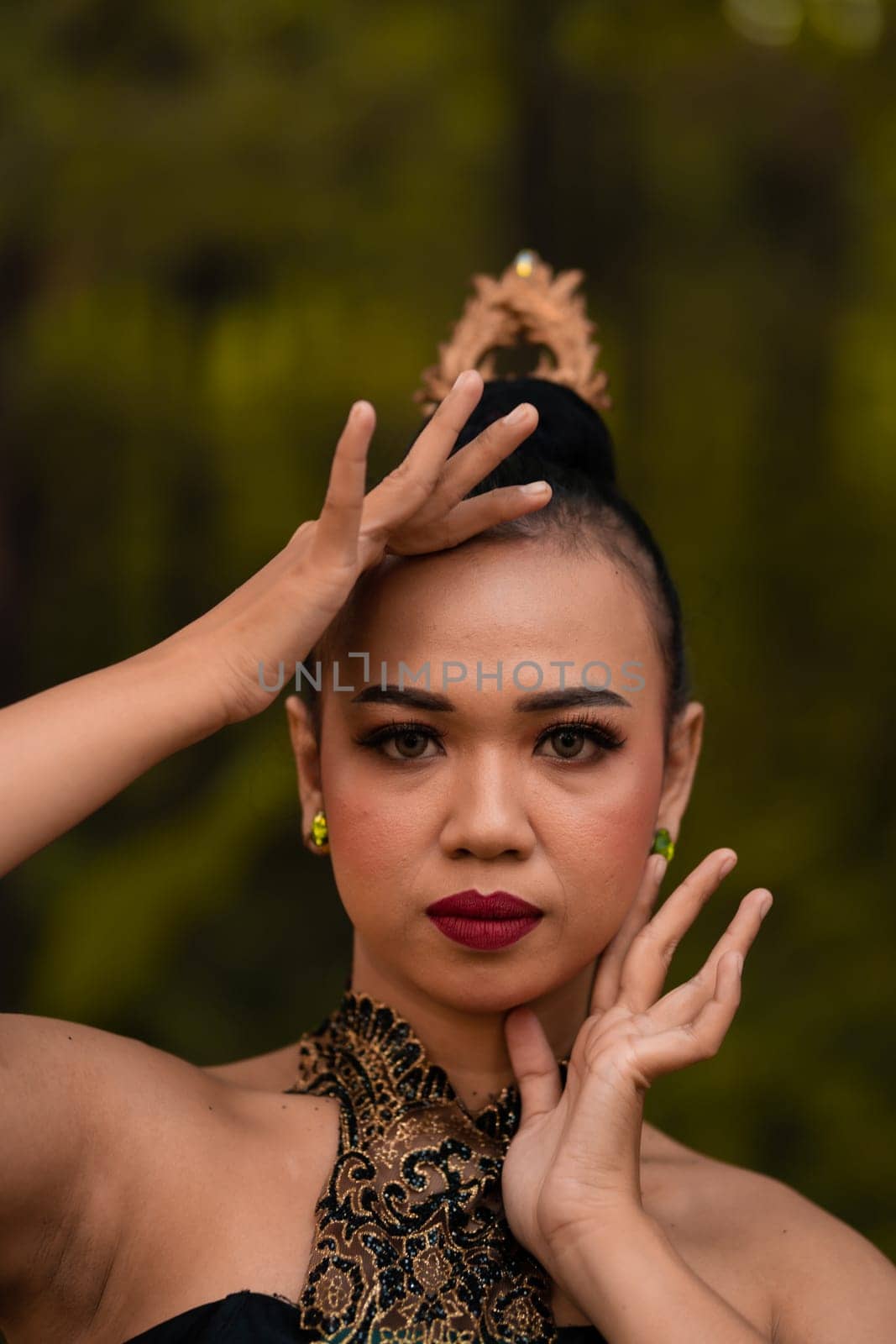 Brave Face of an Asian woman in a traditional green costume with golden accessories on her body during the competition in a dance festival in front of the forest