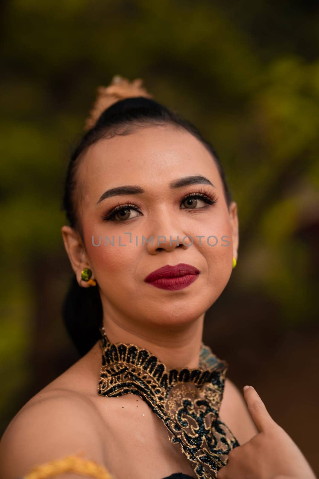 Close-up face of an Asian woman in makeup with red lips and a golden black necklace inside the forest