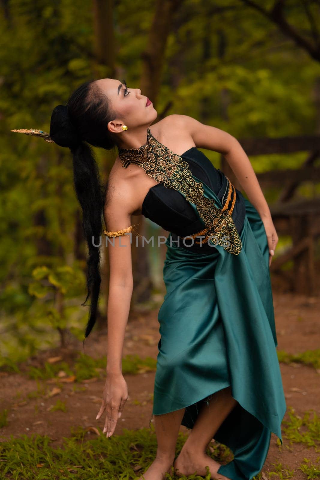 An Indonesian woman poses with black hair dangling to the ground while wearing a green dance costume inside the forest