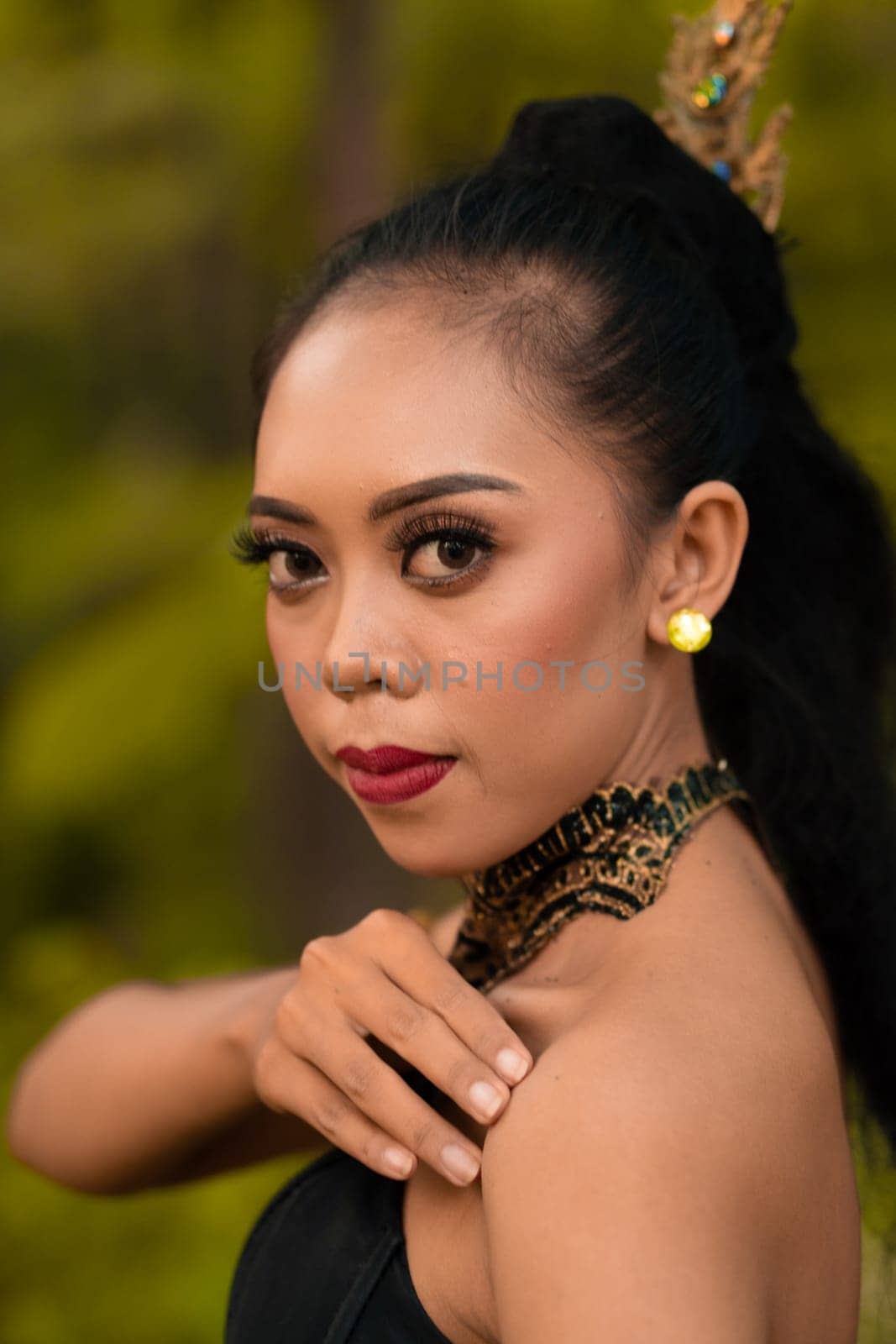 Portrait of a mystical woman in makeup with black hair and wearing a gold jewelry in front of the forest