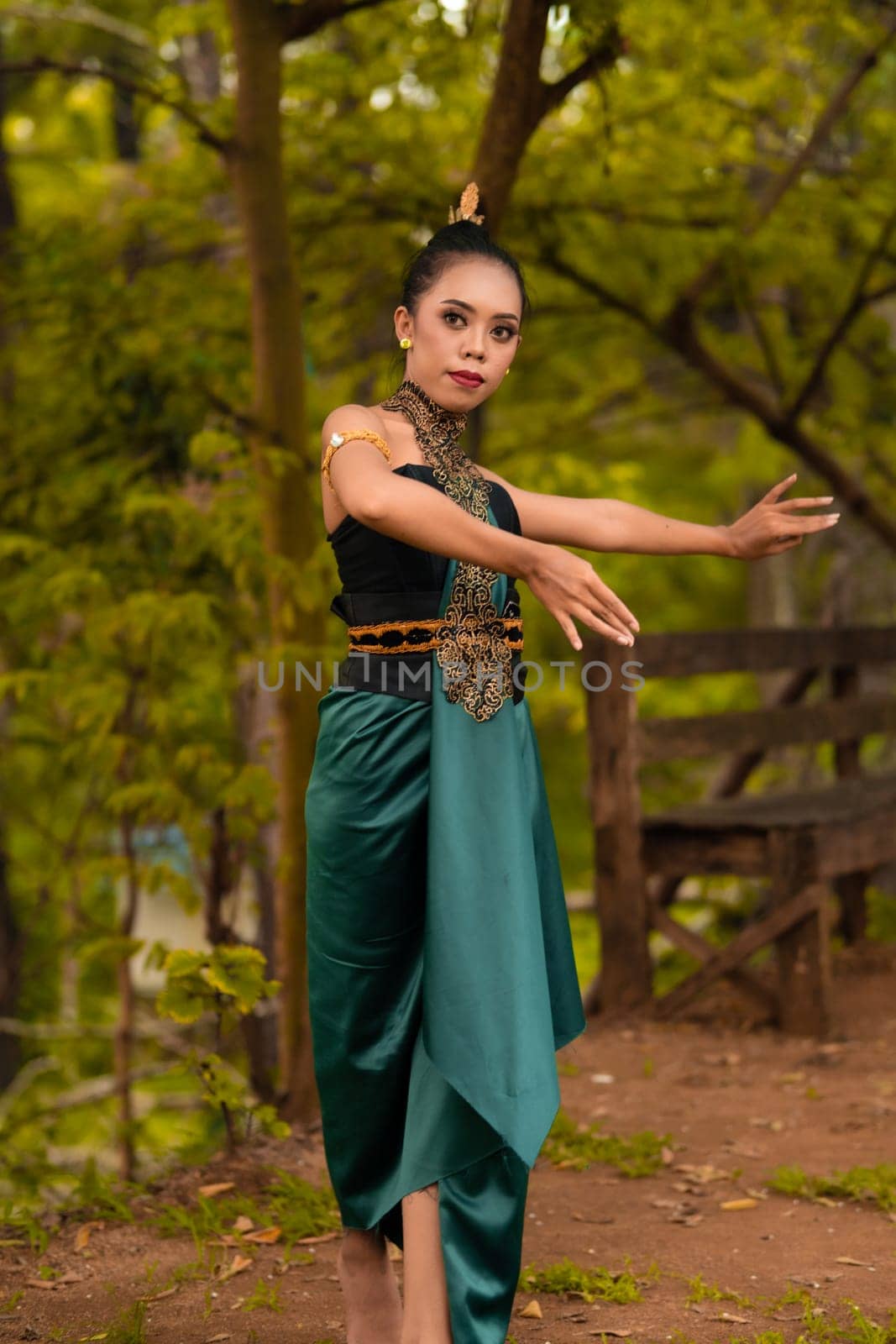 Javanese woman dancing in front of the woods in green costume while in makeup and performing at the village