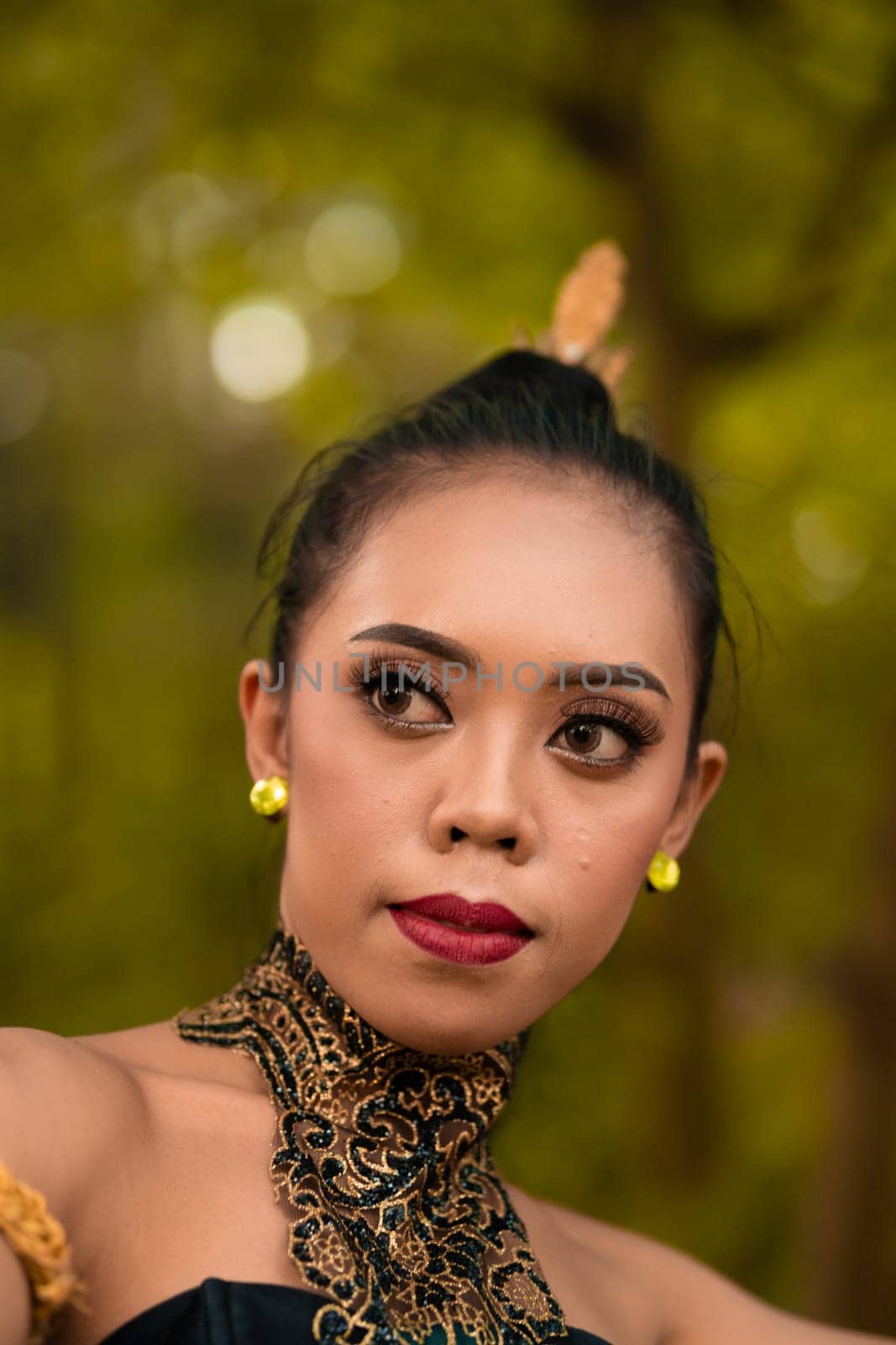 Portrait of a beautiful Asian woman in makeup while dancing in front of the jungle with a black and green costume on her body during the daylight