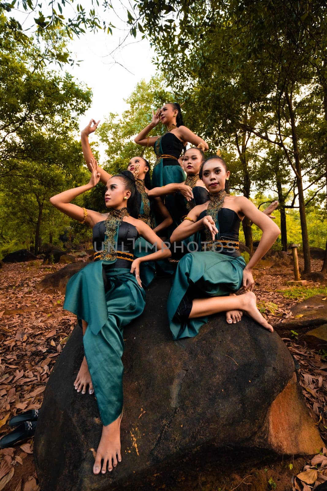 A Group of Asian people in green costumes sitting on a big rock with brown leaves in the background inside the forest