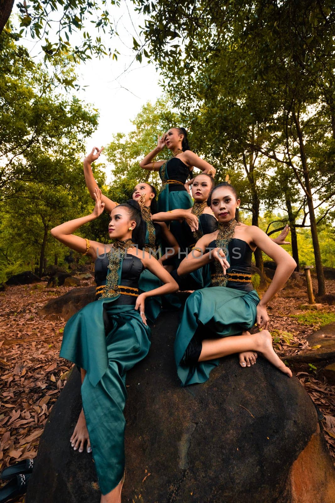 A Group of Asian people in green costumes sitting on a big rock with brown leaves in the background inside the forest