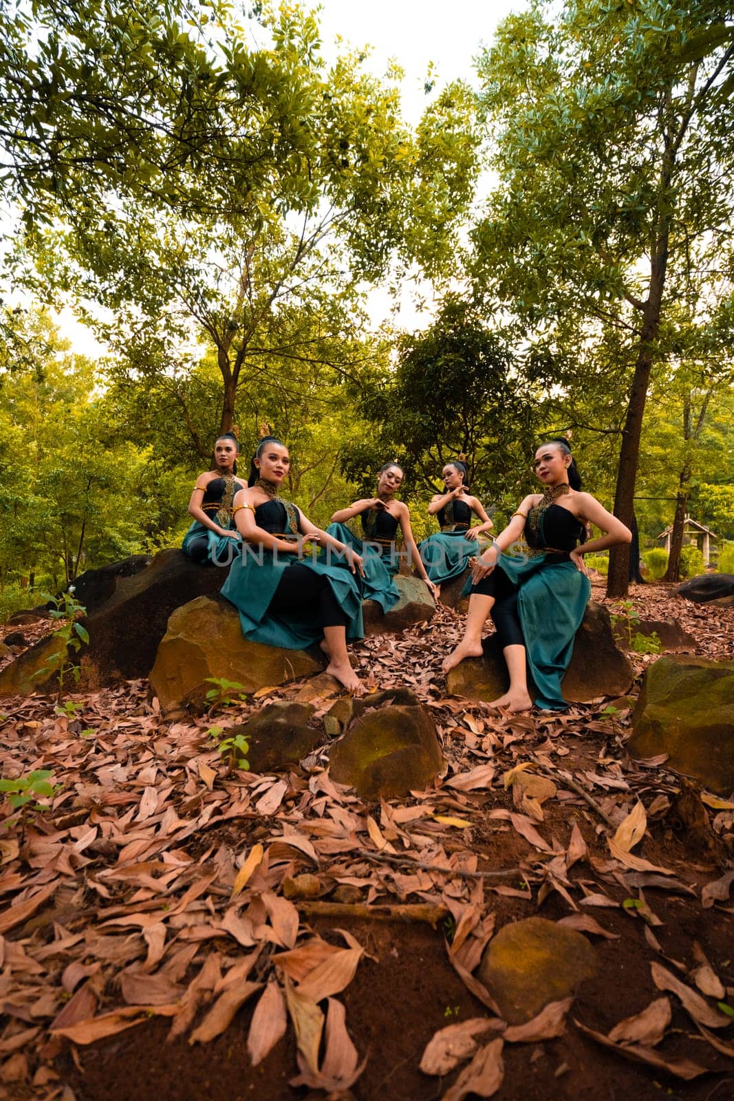 A Group of Asian women takes a vacation to the forest while wearing a green skirt and sitting on a rock during the morning