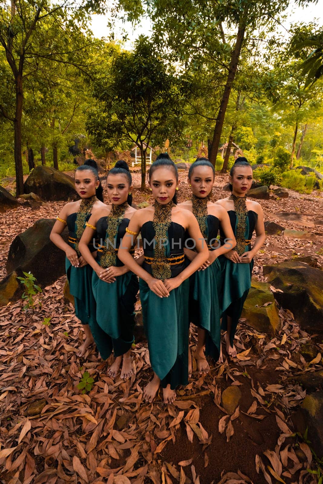Glamor Asian women with green costumes and makeup line up together in the jungle with brown leaves on the ground