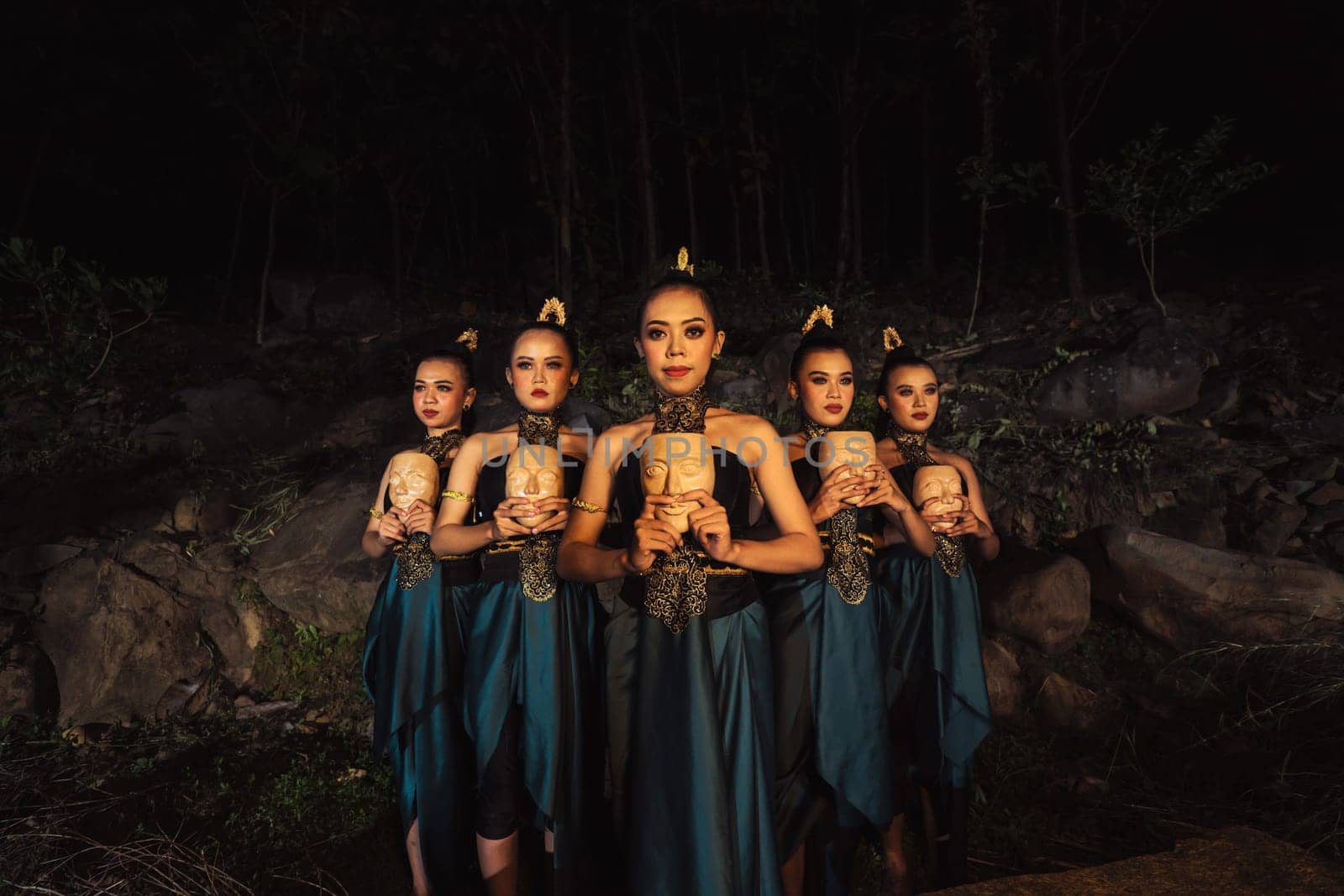 A Group of ethnical women holding a wooden craft mask in their hands while in line inside the wood in the night