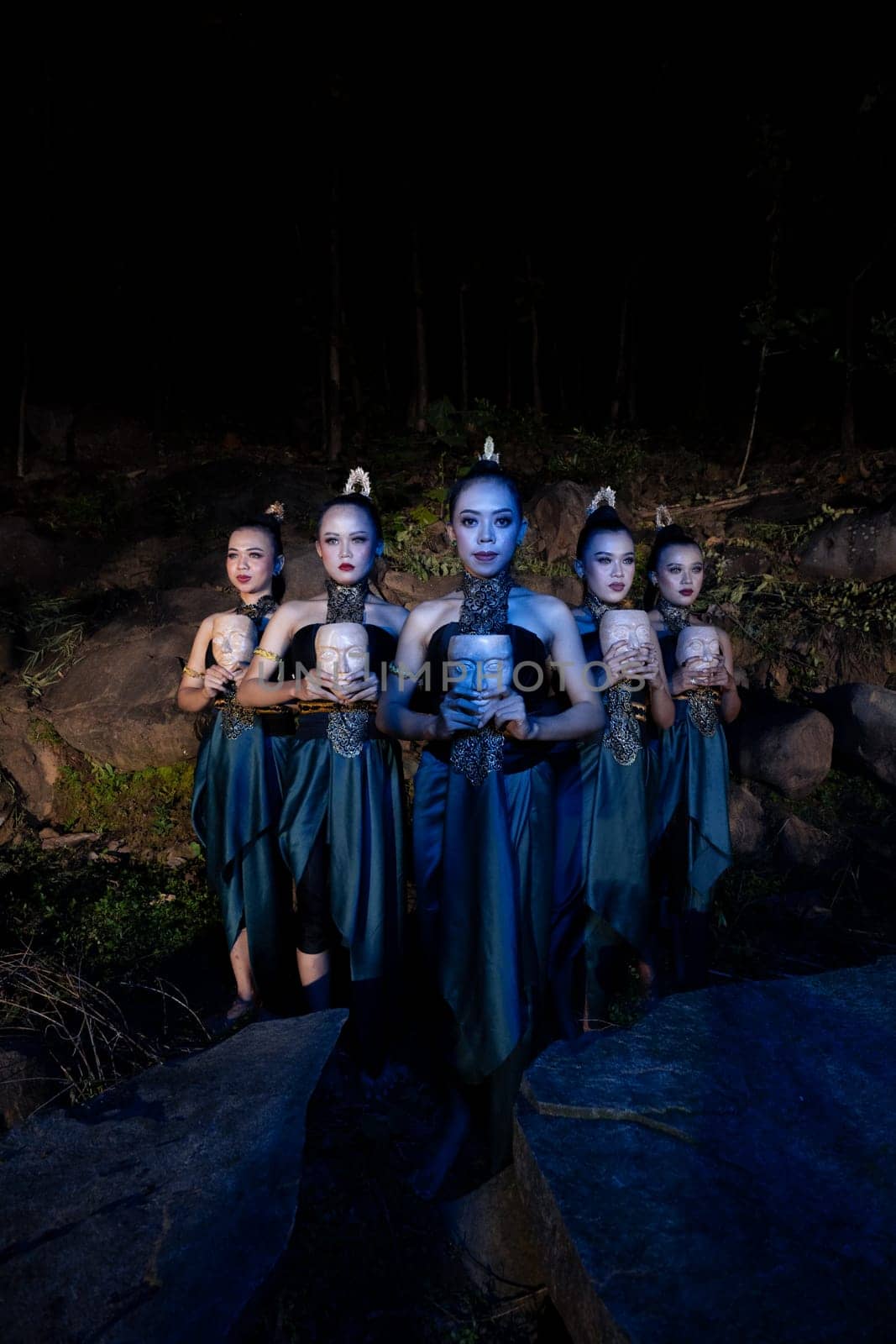 A Group of Balinese woman line up with the wooden mask in their hands while wearing a traditional dance costumes in the night