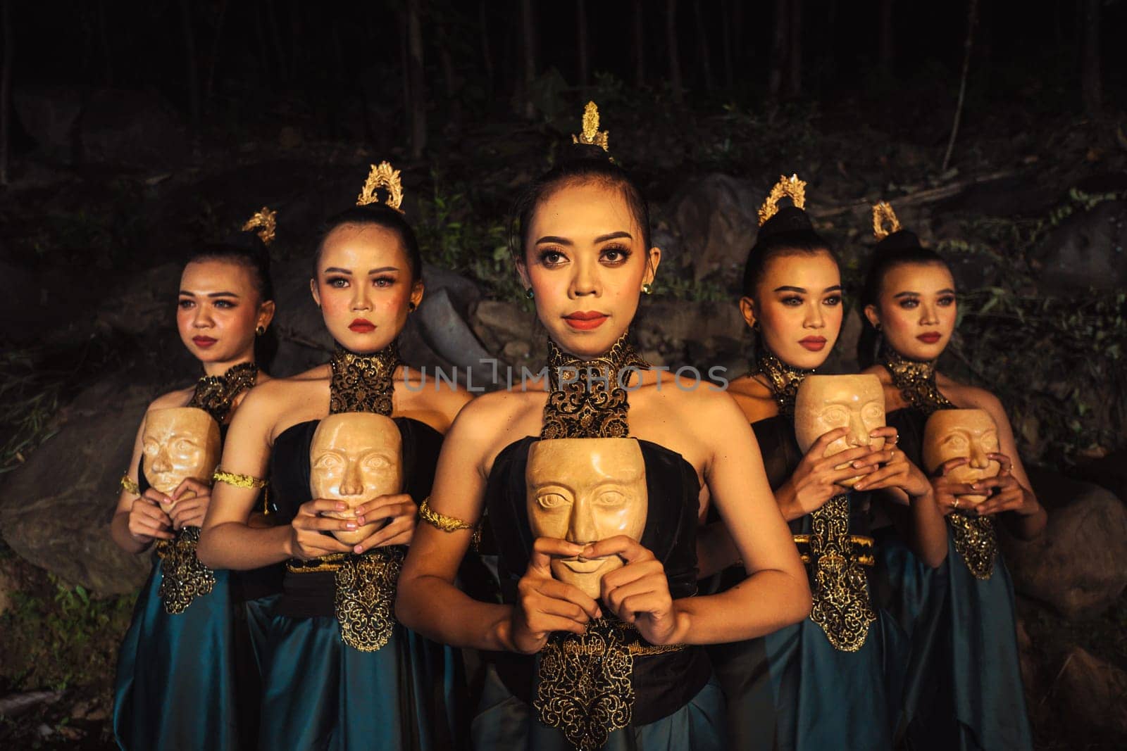 A Group of ethnical women holding a wooden craft mask in their hands while in line inside the wood in the night