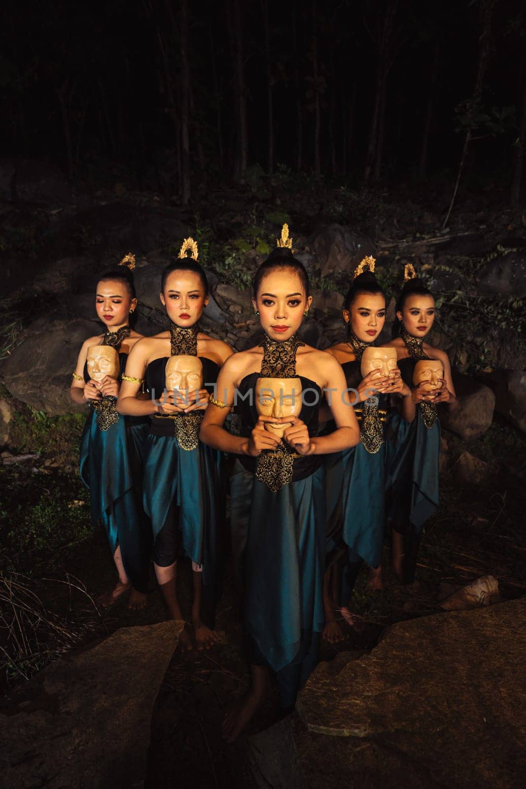 A Group of ethnical women holding a wooden craft mask in their hands while in line inside the wood in the night