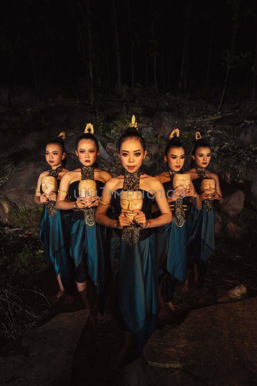 A Group of ethnical women holding a wooden craft mask in their hands while in line inside the wood in the night