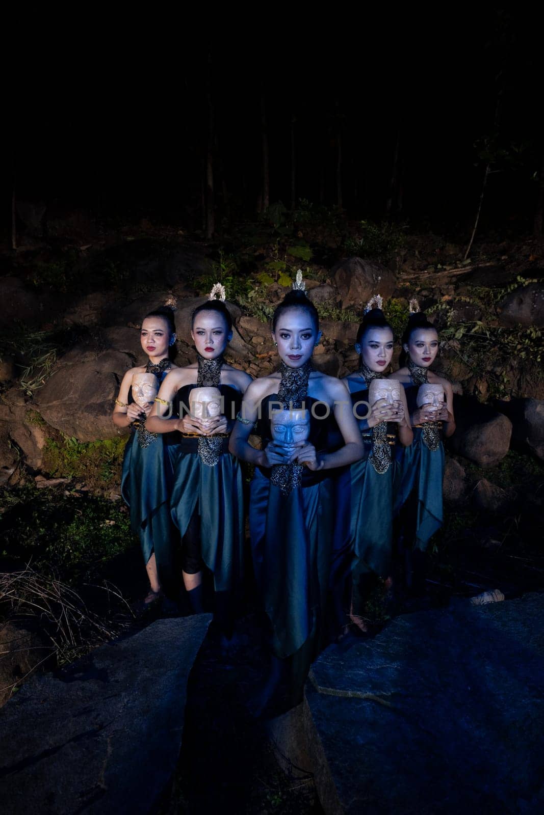 A Group of Balinese woman line up with the wooden mask in their hands while wearing a traditional dance costumes in the night