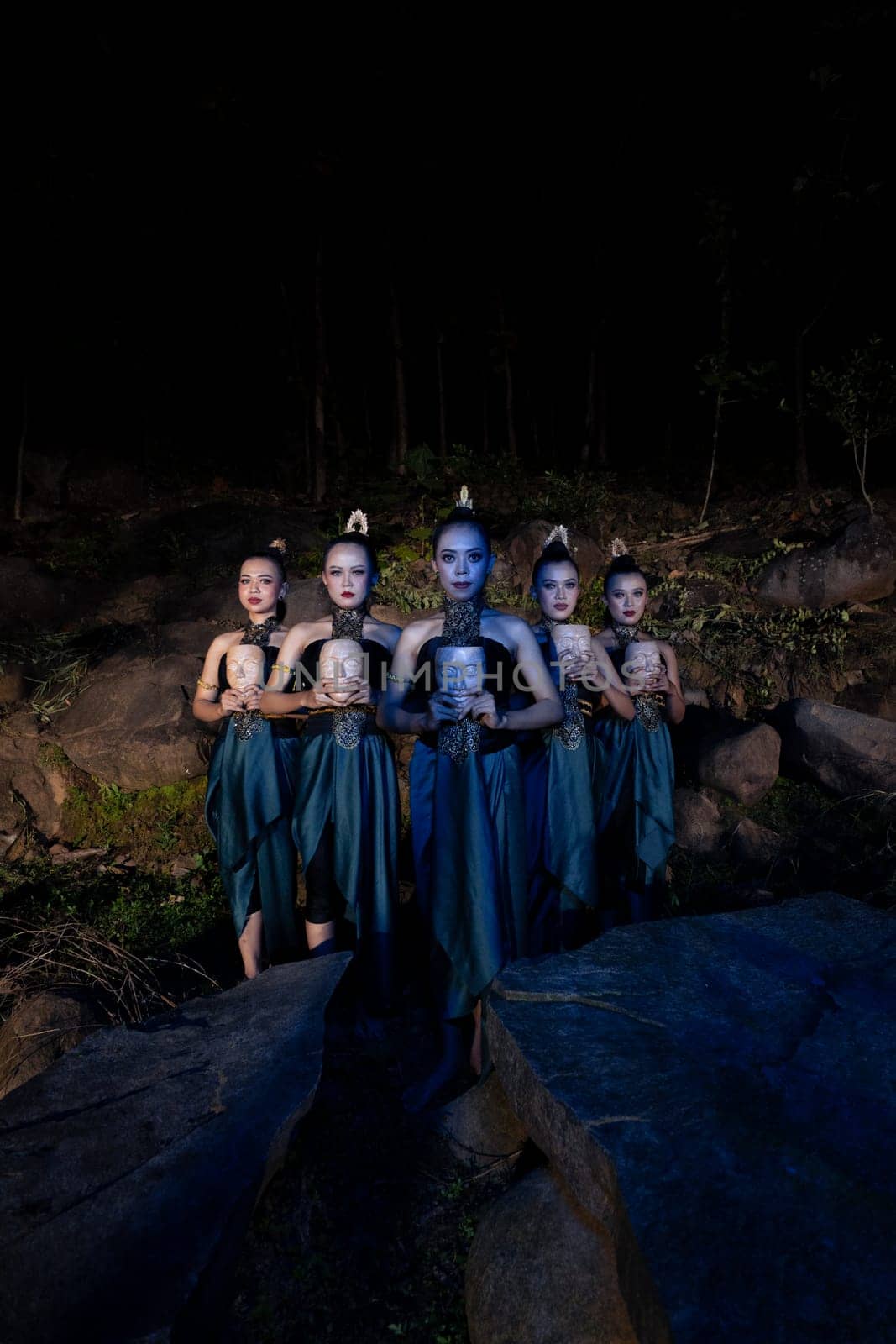 A Group of Javanese women standing in the woods between the rocks while holding a wooden mask inside the village