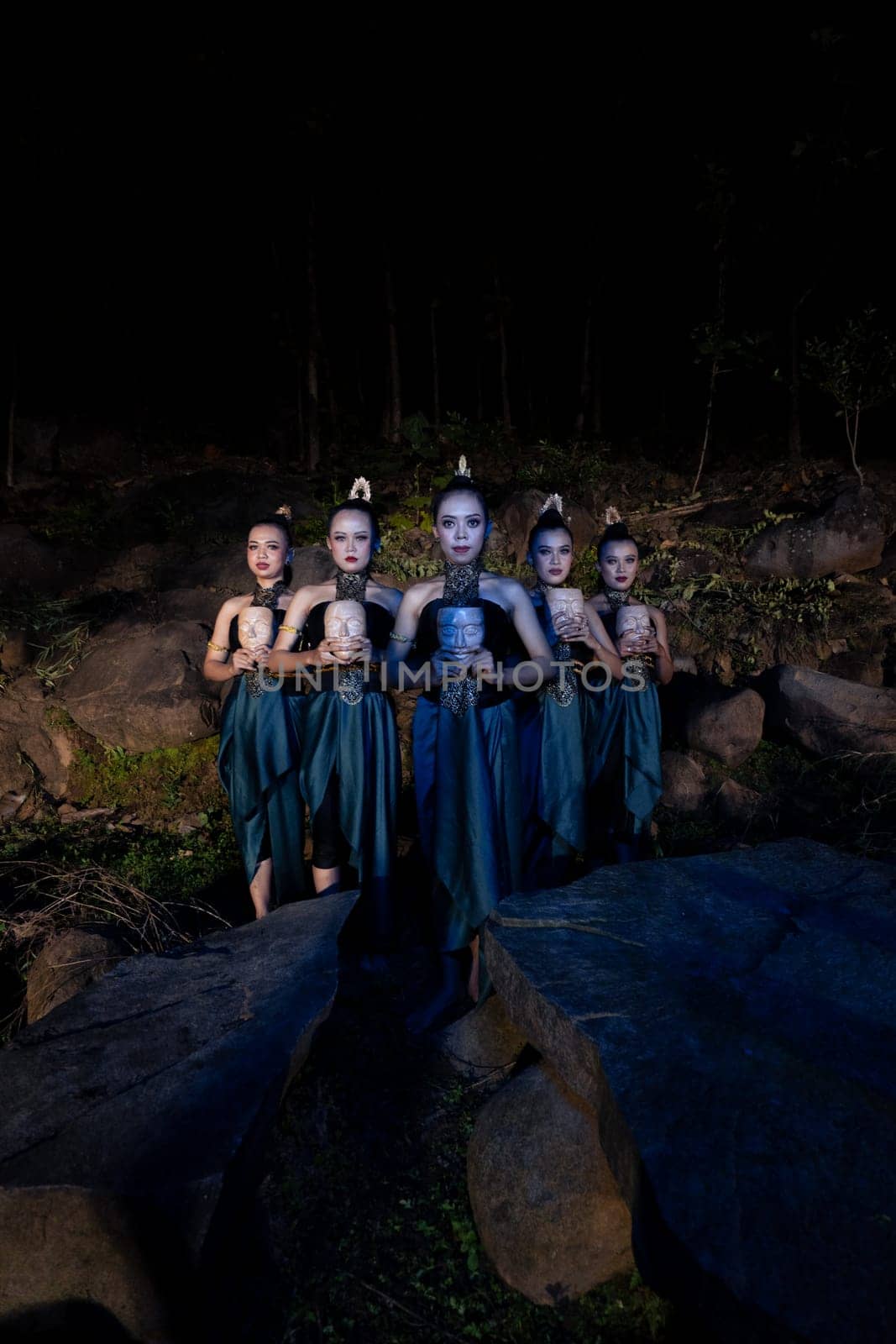 A Group of Javanese women standing in the woods between the rocks while holding a wooden mask inside the village