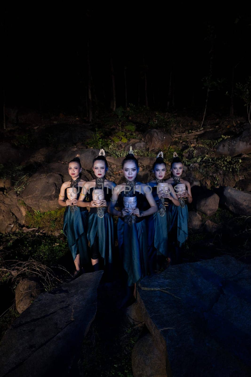 A Group of Javanese women standing in the woods between the rocks while holding a wooden mask inside the village