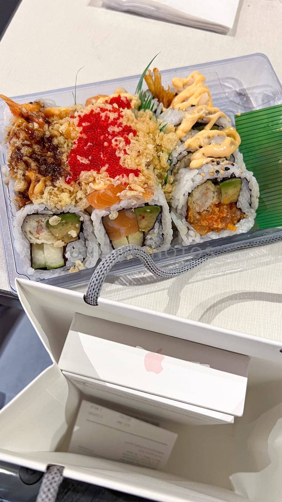 Ottawa, ON Canada - March 11, 2025: Assorted sushi rolls including salmon, avocado, and crab accompanied by bag with box of new iPhone smartphone purchase