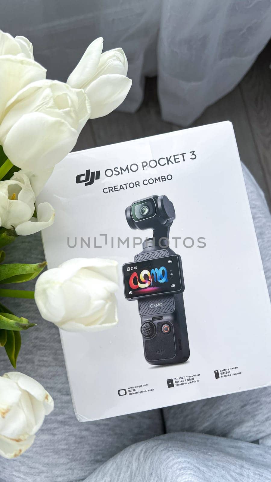 Ottawa, Canada - April 05, 2025: The DJI Osmo Pocket 3 Creator Combo packaging is elegantly placed on a soft gray surface, surrounded by fresh white tulips, innovative design for content creators