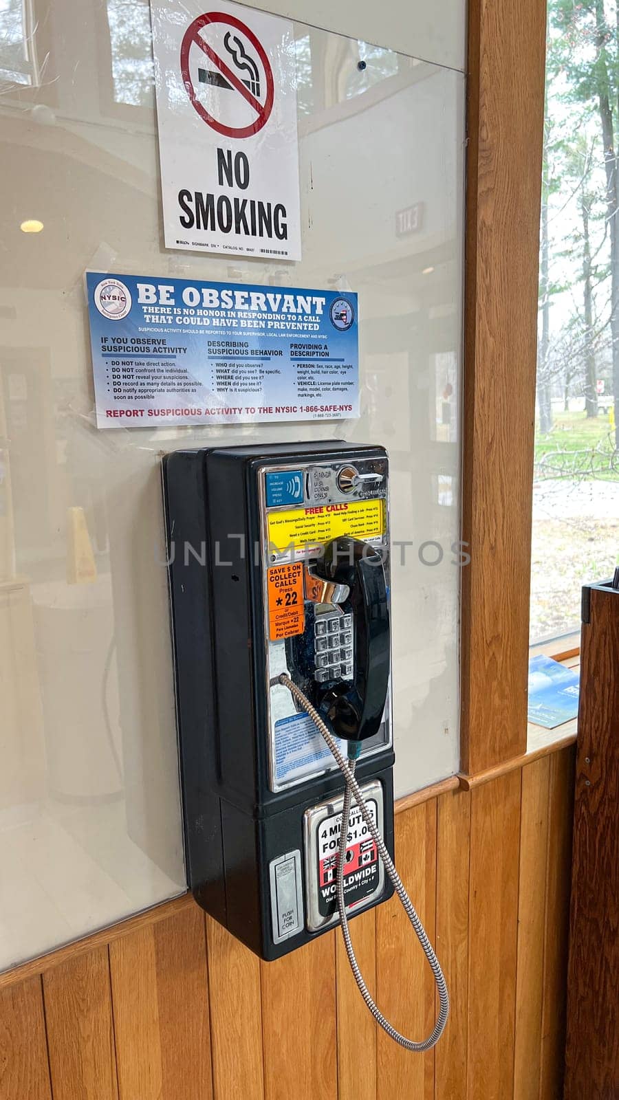 Syracuse, NY USA - March 04, 2025: Classic payphone installed on a wooden wall in a public area, featuring a no smoking sign and an observant notice, evoking nostalgia for traditional communication method