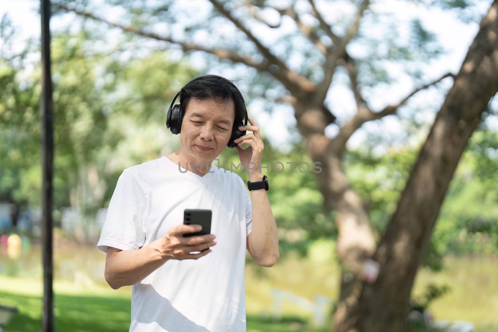 An elderly man checks his smartphone while listening to music, highlighting wellness and connectivity in a natural setting.