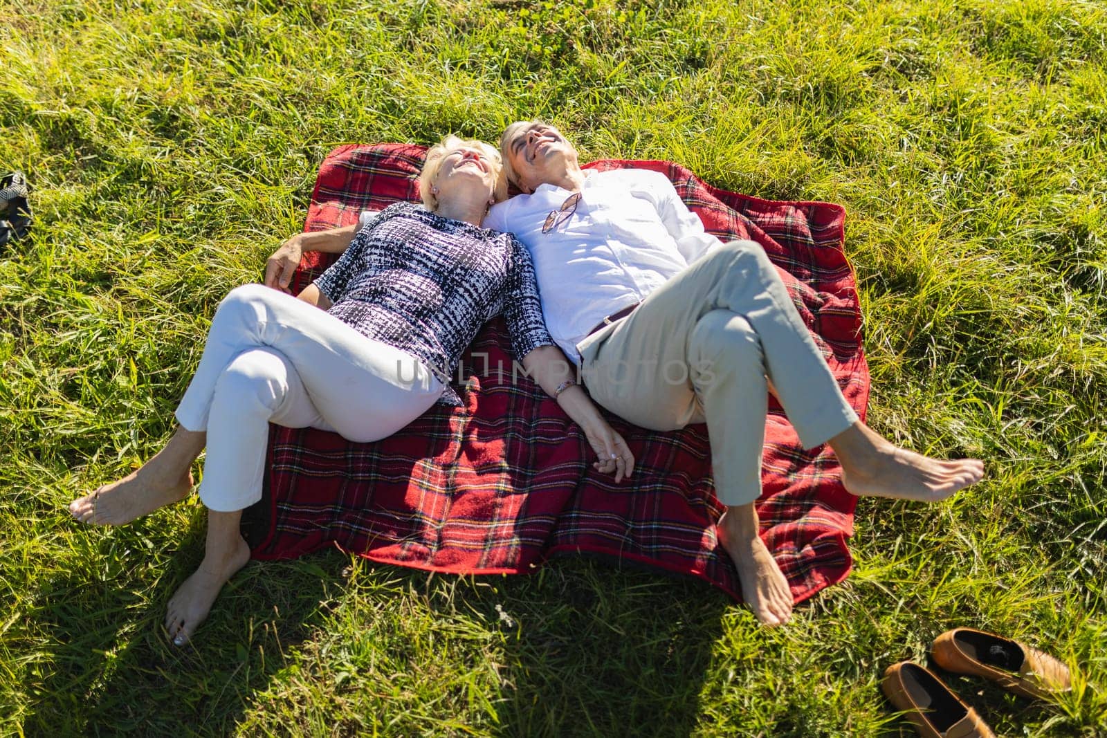 Retired couple lying on a blanket in a meadow, enjoying a relaxing day together