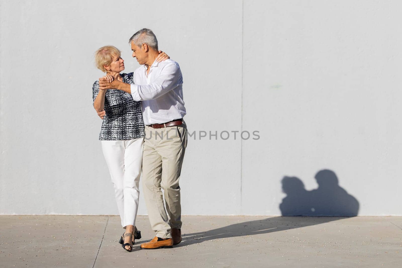 Happy mature couple dancing outdoors in the sun, enjoying retirement and active lifestyle