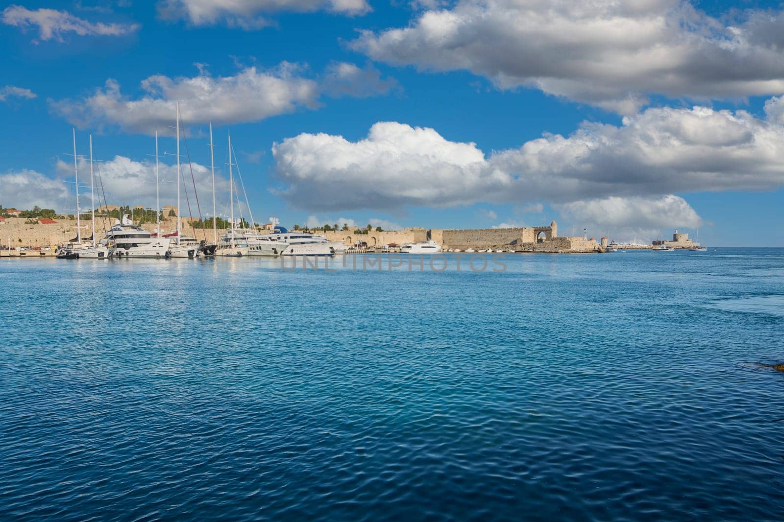 Crete.Greece may 15, 2025: picturesque rhodes marina on a sunny day with yachts, clear blue water, and historic fortifications, creating a serene and inviting atmosphere.