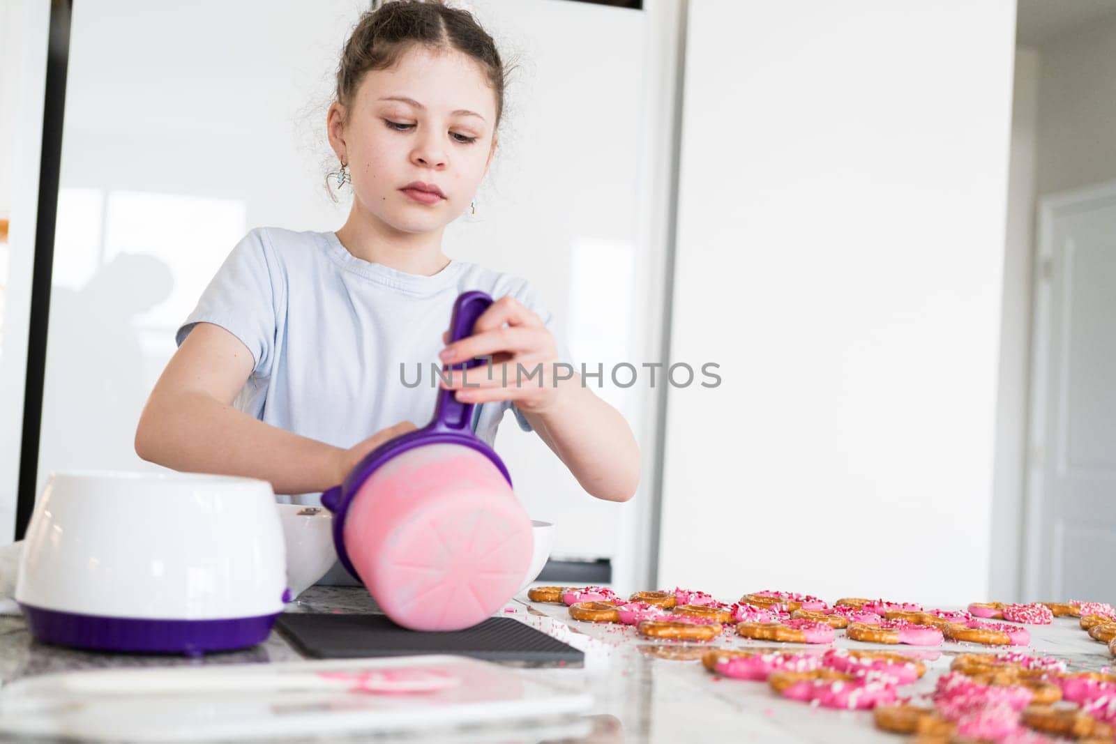 With focused attention, this budding culinary artist dips pretzels into a pot of melted chocolate, creating sweet delights in the warmth of a well-lit home kitchen.