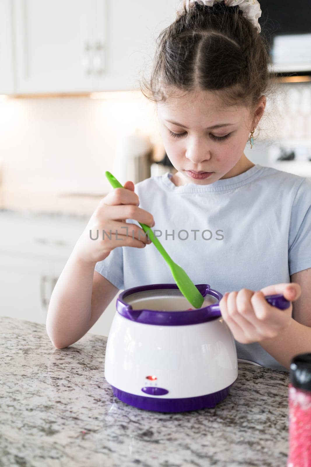 With focused attention, this budding culinary artist dips pretzels into a pot of melted chocolate, creating sweet delights in the warmth of a well-lit home kitchen.