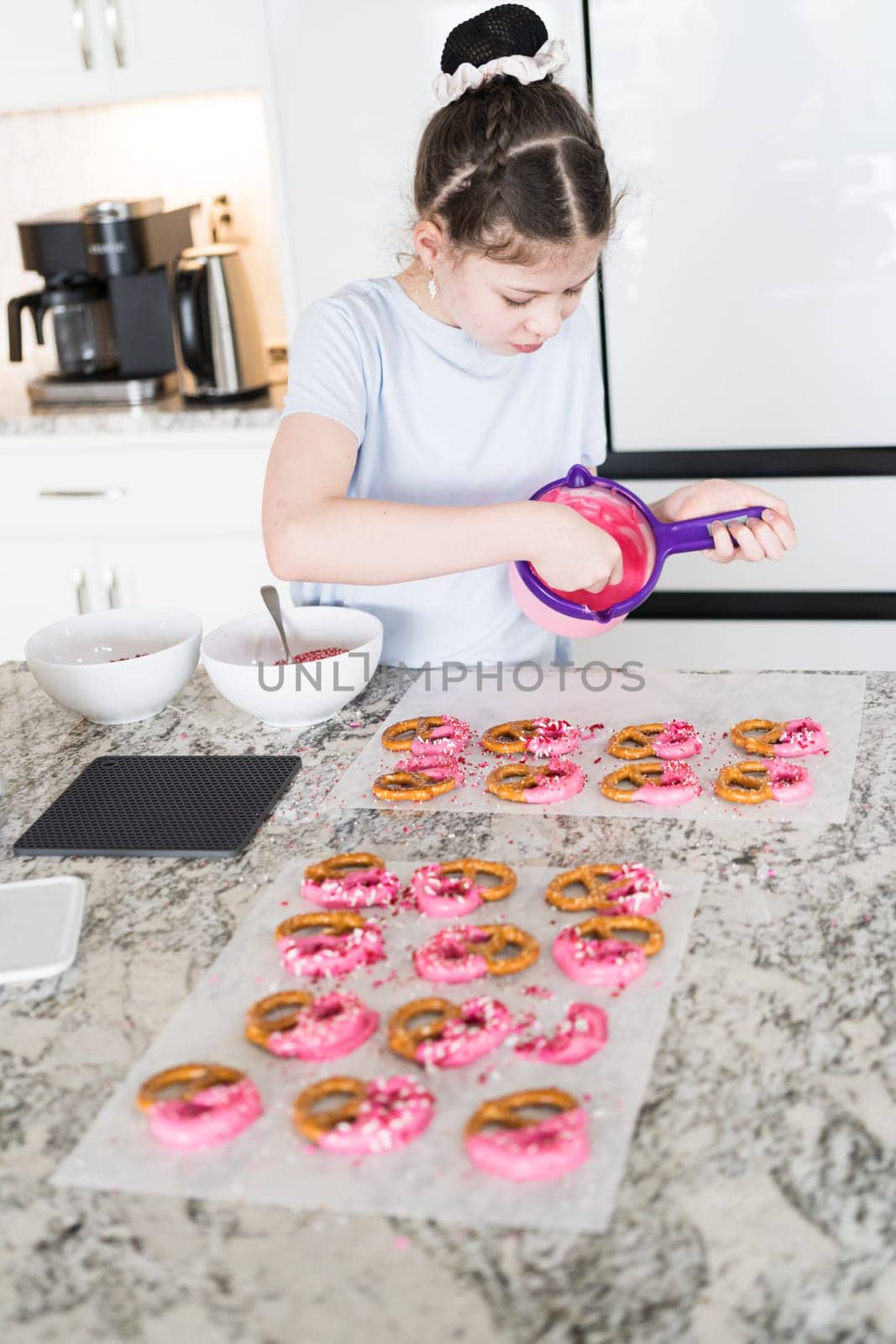 With focused attention, this budding culinary artist dips pretzels into a pot of melted chocolate, creating sweet delights in the warmth of a well-lit home kitchen.